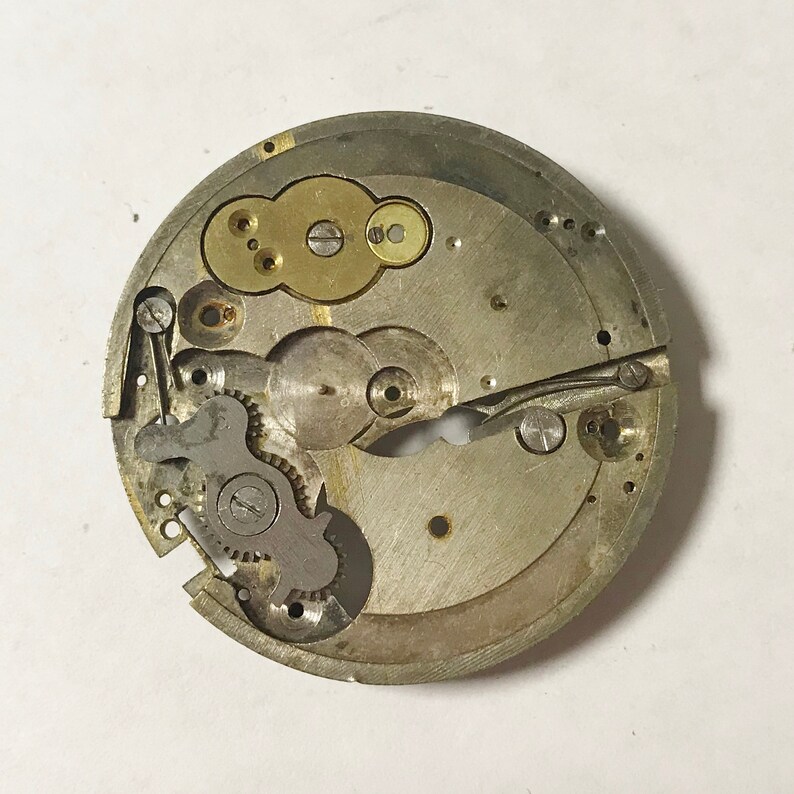 Op de afbeelding: Close-up van een zilveren uurwerk met tandwielen en een goudkleurig opwindmechanisme.