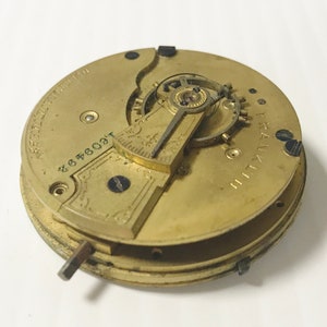May include: A gold-toned pocket watch movement with intricate gears and a winding key. The watch face is marked "FRANKLIN" and has the number "2646091".