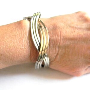 May include: A silver and gold toned bangle bracelet with a woven design.