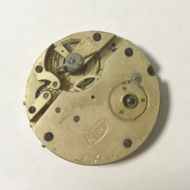 May include: Close-up of a gold-toned pocket watch movement with the inscription "L.B. & S.  Great  London  No. 220910".