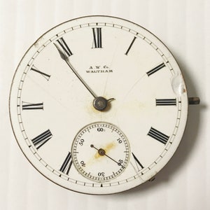May include: Antique pocket watch face with a white background, black Roman numerals, and a smaller seconds dial. The watch face has the text "A.W. Co. WALTHAM" and shows signs of age and wear.