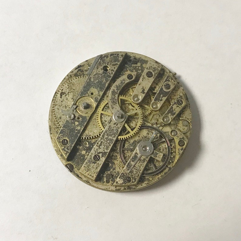 May include: Close-up of a vintage pocket watch movement with intricate gears and levers. The metal is aged and has a worn patina.