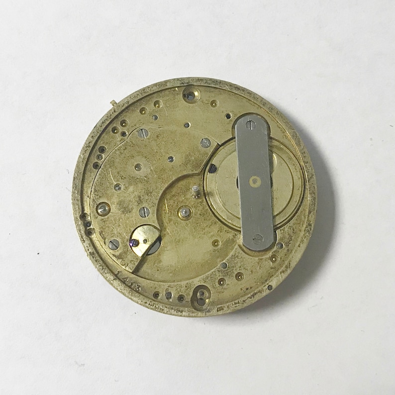 May include: Close-up of a gold-toned watch movement with intricate gears and a silver lever. The movement is exposed, showing the inner workings of the watch.