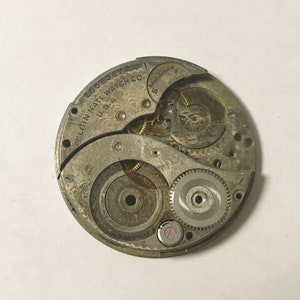 K&ouml;nnte beinhalten: Nahaufnahme des Innenlebens einer silbernen Taschenuhr. Das Zifferblatt der Uhr ist mit "ELGIN NATL WATCH CO. U.S.A. 28653879" beschriftet.
