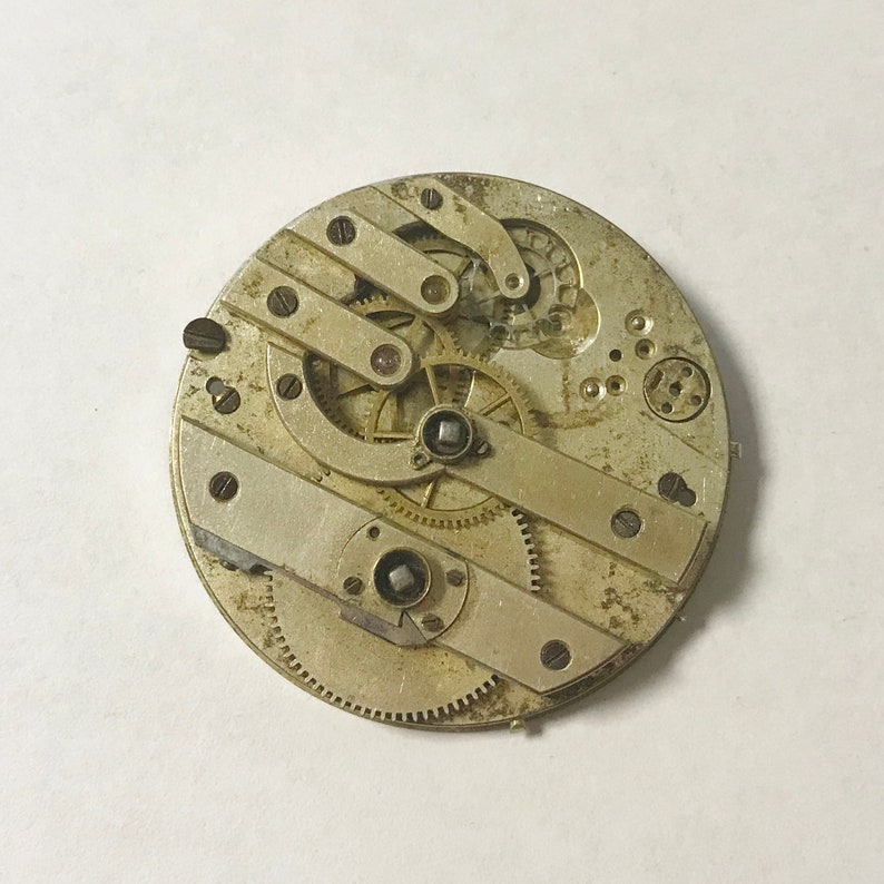 Puede incluir: Primer plano de un movimiento de reloj plateado con engranajes y palancas intrincados. El movimiento est&aacute; expuesto y muestra el funcionamiento interno del reloj.
