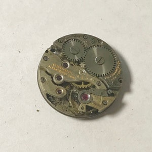 May include: Close-up of a silver watch movement with gears and a red jewel. The movement is labeled "TOLEDO WATCH CO. 16 JEWELS ADJUSTED"