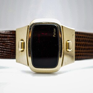 May include: A gold-toned Pulsar digital watch with a brown leather strap. The watch face is a dark red LED display.