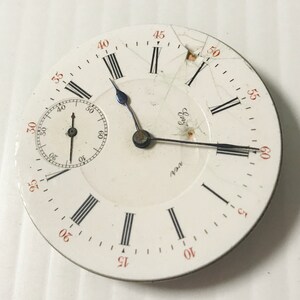 Puede incluir: Una esfera de reloj de bolsillo blanca con marcadores de hora en n&uacute;meros romanos negros y marcadores de minutos negros. La esfera del reloj tiene un peque&ntilde;o subdial circular en la posici&oacute;n de las 12 en punto. La esfera del reloj est&aacute; agrietada y le falta un peque&ntilde;o trozo de cristal. La esfera del reloj tiene las palabras "ver" y "Eng" impresas.