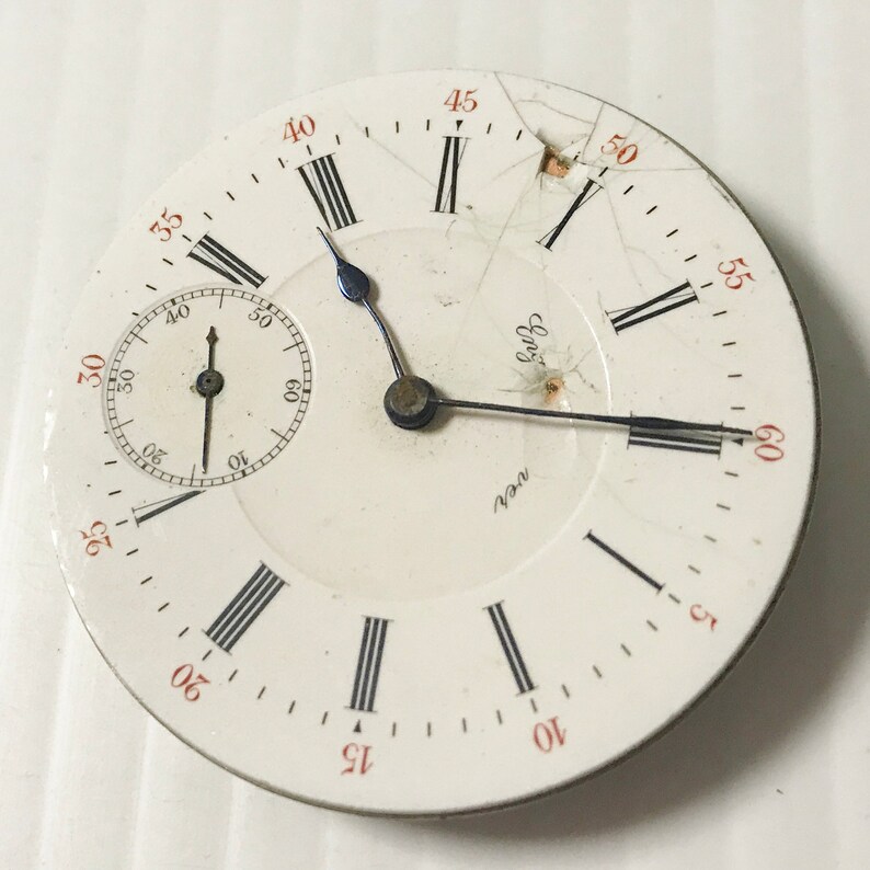 Puede incluir: Una esfera de reloj de bolsillo blanca con marcadores de hora en n&uacute;meros romanos negros y marcadores de minutos negros. La esfera del reloj tiene un peque&ntilde;o subdial circular en la posici&oacute;n de las 12 en punto. La esfera del reloj est&aacute; agrietada y le falta un peque&ntilde;o trozo de cristal. La esfera del reloj tiene las palabras "ver" y "Eng" impresas.