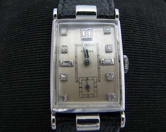May include: A silver rectangular wristwatch with a white face and diamond accents. The watch has a black leather band.