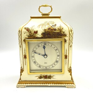 May include: A white and gold mantle clock with a floral design and a Roman numeral clock face. The clock face reads "Gilbert London".