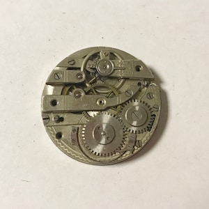 Puede incluir: Primer plano de un movimiento de reloj plateado con engranajes intrincados y una palanca de ajuste "R&Aacute;PIDO LENTO". El movimiento est&aacute; etiquetado como "SWISS".