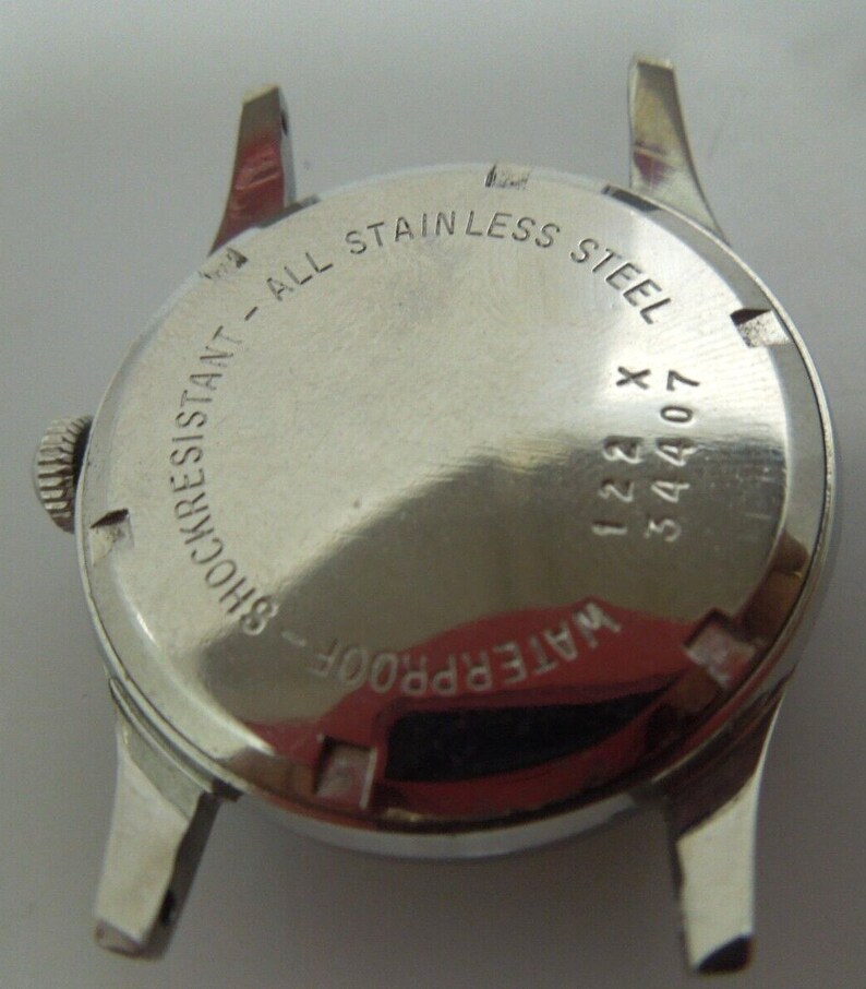 May include: The back of a silver wristwatch with the text "WATERPROOF - SHOCKRESISTANT - ALL STAINLESS STEEL" and the numbers "34407 122 X" engraved on the case.