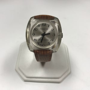 Peut inclure: Une montre-bracelet en cuir marron avec un bo&icirc;tier en plastique transparent. Le cadran de la montre est blanc avec des chiffres et des aiguilles noirs. Le cadran de la montre comporte &eacute;galement le texte "PRINCETON" et "SWISS MOVEMENT".