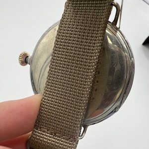May include: A silver pocket watch with a brown fabric strap. The watch face is visible and has a decorative design.