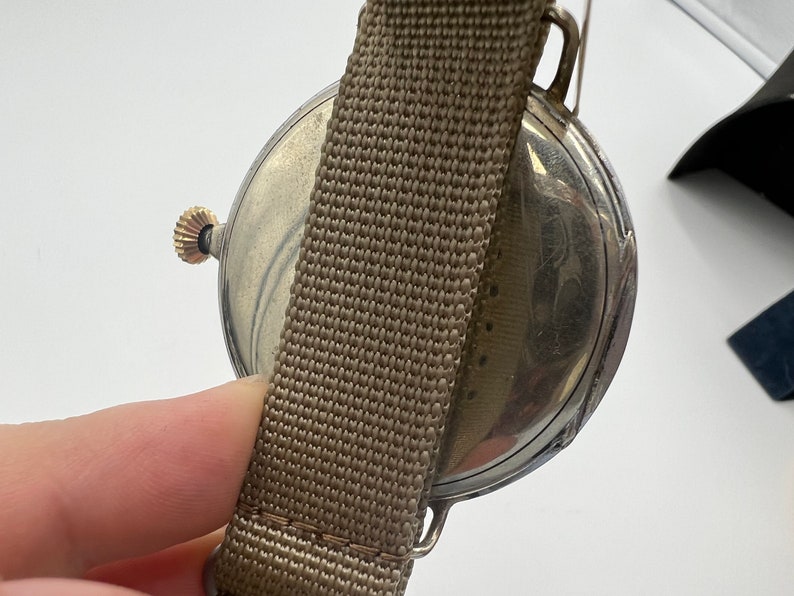 May include: A silver pocket watch with a brown fabric strap. The watch face is visible and has a decorative design.