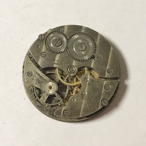 May include: Close-up of a silver pocket watch movement with the inscription "LANGENDORF" and "SUISSE" on the face. The watch has a variety of gears and springs visible.