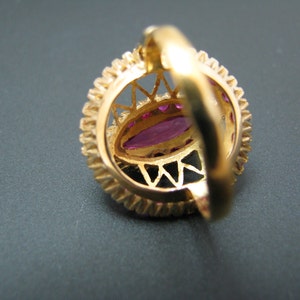 May include: A gold ring with a large, oval-shaped, pink gemstone surrounded by smaller, round, pink gemstones. The ring has a delicate, intricate design.