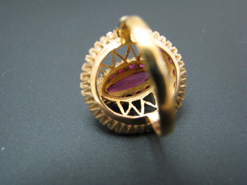 May include: A gold ring with a large, oval-shaped, pink gemstone surrounded by smaller, round, pink gemstones. The ring has a delicate, intricate design.