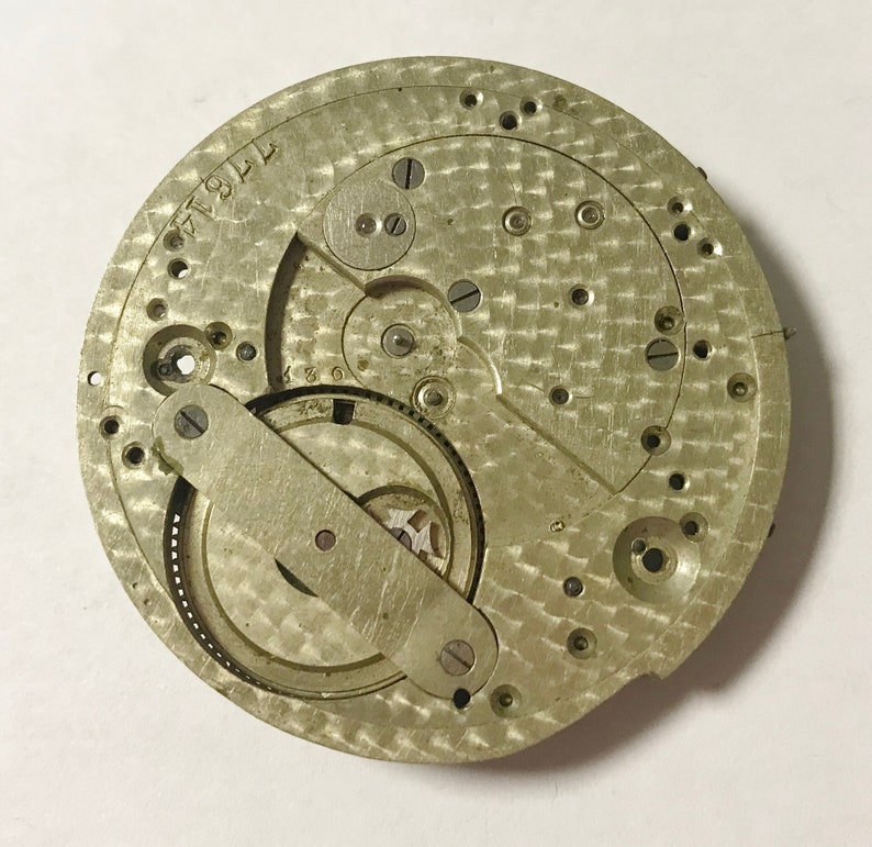 Pu&ograve; includere: Primo piano di un movimento di orologio argentato con ingranaggi intricati e una superficie testurizzata. Il movimento &egrave; etichettato "17914".