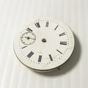Puede incluir: Esfera de reloj de bolsillo blanca con marcadores de hora en n&uacute;meros romanos y un dial de segundero circular m&aacute;s peque&ntilde;o. La esfera del reloj tiene un aspecto desgastado y envejecido con ara&ntilde;azos visibles.