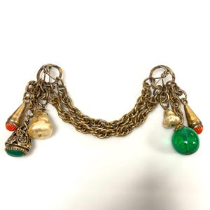 May include: A vintage gold-tone chain with decorative charms. The charms include pear-shaped beads, green and red accents, and ornate filigree details. The chain is connected by two circular clasps.