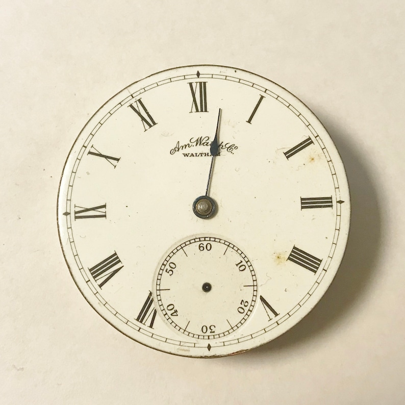 May include: A white pocket watch with Roman numeral hour markers and a smaller, concentric circle with minute markers. The watch face has the text "Am. Watch Co. WALTHAM" printed on it.