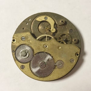 K&ouml;nnte beinhalten: Nahaufnahme eines goldfarbenen Uhrwerks mit mehreren Zahnr&auml;dern und einer Aufzugsfeder. Das Uhrwerk ist freigelegt und zeigt die komplizierte Funktionsweise der Uhr.