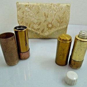May include: A vintage gold-toned makeup compact with a floral patterned fabric case. The compact contains two lipstick tubes and a small bottle with a white lid.