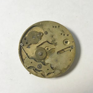 Pu&ograve; includere: Primo piano di un movimento di orologio vintage, che mostra ingranaggi, molle e leve intricati. I componenti color ottone sono disposti all'interno di una cornice circolare, rivelando la complessit&agrave; meccanica dell'orologio. Il design include piccole viti e varie parti funzionali.