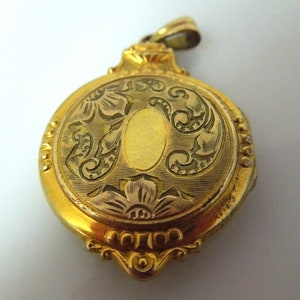 May include: A gold-toned locket with an engraved floral design. The locket has a hinged lid and a small loop at the top for attaching a chain.