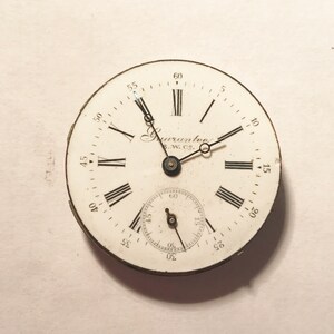 Puede incluir: Una esfera de reloj de bolsillo blanca con marcadores de hora en n&uacute;meros romanos negros y marcadores de minutos negros. La esfera del reloj tiene un peque&ntilde;o dial de segundos en la parte inferior. La esfera del reloj est&aacute; etiquetada como "Guarantee E.W. Co."