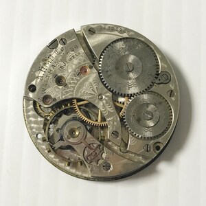 May include: Close-up of a silver pocket watch movement with intricate gears and a decorative design. The watch is labeled "Waltham Watch Co. Waltham Mass. 15 Jewels."
