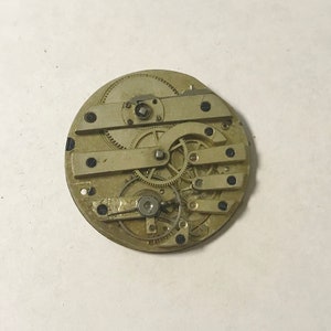 May include: Close-up of a gold-toned pocket watch movement with intricate gears and levers.