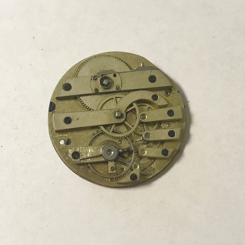 May include: Close-up of a gold-toned pocket watch movement with intricate gears and levers.