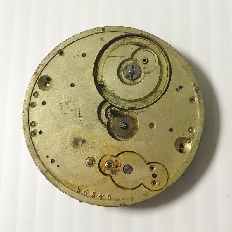 K&ouml;nnte beinhalten: Nahaufnahme eines goldfarbenen Taschenuhrwerks mit komplizierten Zahnr&auml;dern und einem kreisf&ouml;rmigen Design. Das Zifferblatt der Uhr fehlt und die R&uuml;ckseite des Uhrengeh&auml;uses ist sichtbar.