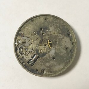 K&ouml;nnte beinhalten: Nahaufnahme eines silbernen Uhrwerks mit freiliegenden Zahnr&auml;dern und einer kleinen Schraube. Das Zifferblatt der Uhr fehlt und die R&uuml;ckseite ist aus Metall.