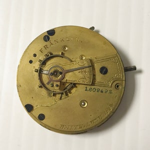May include: Close-up of a gold-colored pocket watch movement with the text "FRANKLIN" and "WALTHAM, MASS." The watch movement has a serial number "1,609492".