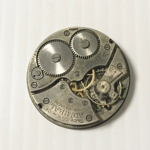 May include: Close-up of a silver pocket watch movement with the text "Tacy Watch Co. Admiral Non-Magnetic 17 Jewels 2 Adjustments 10090378 Swiss" printed on the face.