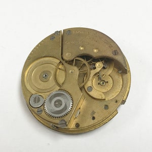 K&ouml;nnte beinhalten: Nahaufnahme eines goldfarbenen Taschenuhrwerks mit der Aufschrift "England Made 15 Jewels Watch Co."