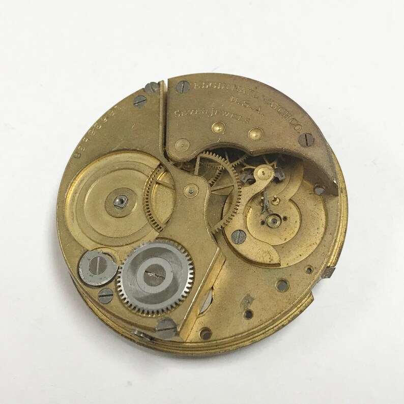 K&ouml;nnte beinhalten: Nahaufnahme eines goldfarbenen Taschenuhrwerks mit der Aufschrift "England Made 15 Jewels Watch Co."