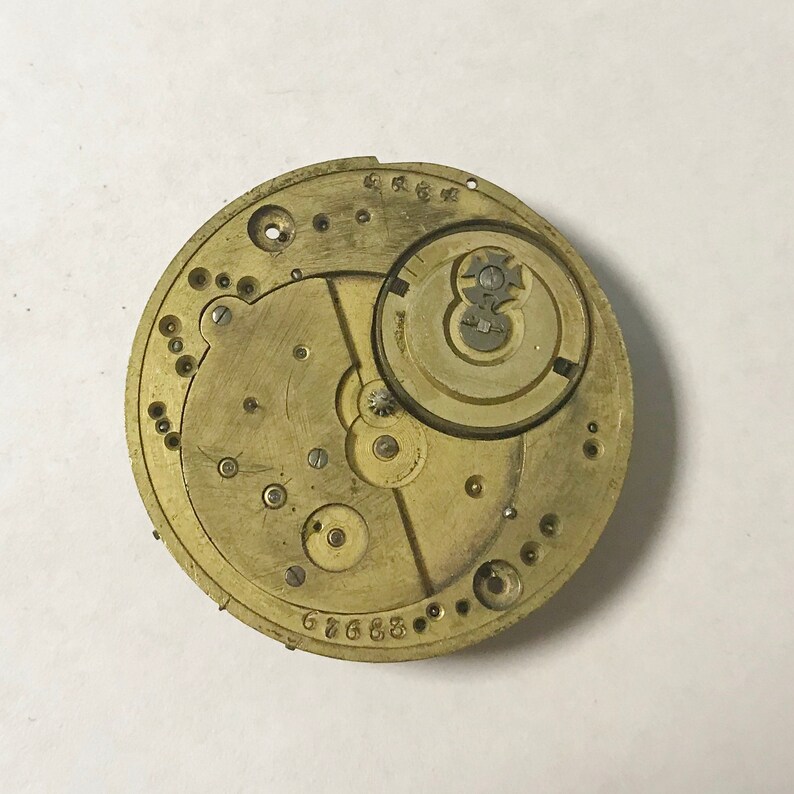 May include: Close-up of a gold-toned watch movement with intricate gears and markings. The movement is labeled "676683".