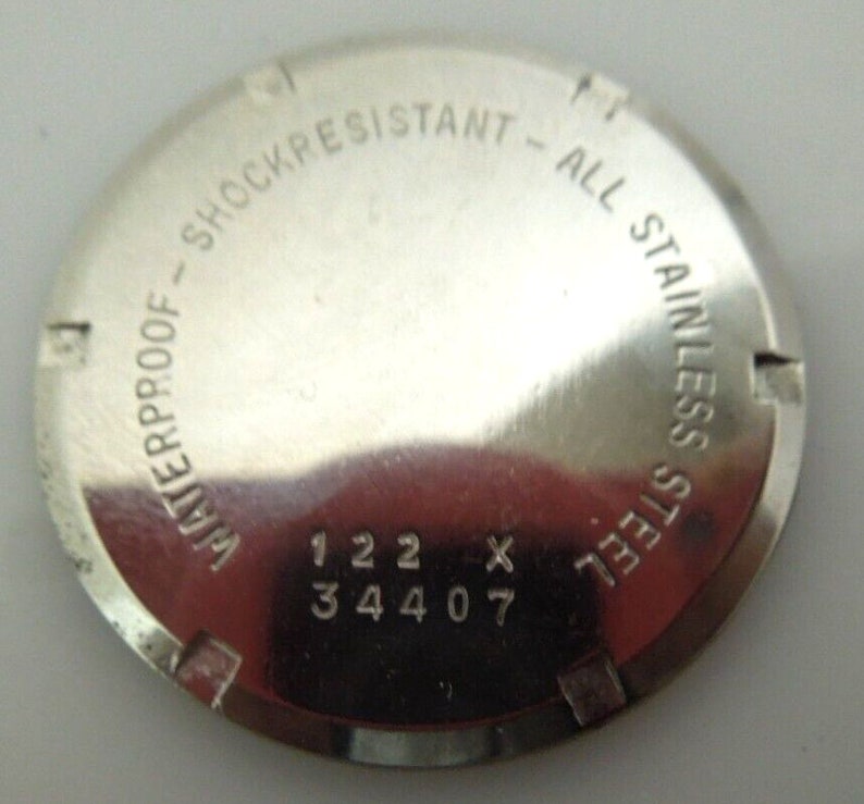 May include: The back of a silver watch with the text "Waterproof - Shockresistant - All Stainless Steel" and the numbers "122 x 344 07".