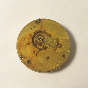 May include: Close-up of the inner workings of a gold-toned pocket watch with the inscription "American Waltham Watch Co." and the serial number "3562085".