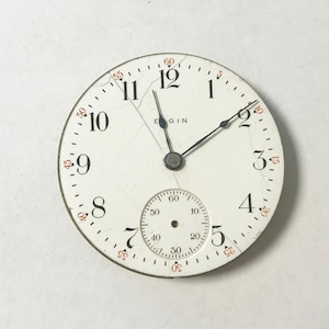 Puede incluir: Una esfera de reloj de bolsillo blanca con agujas negras y marcadores de hora en n&uacute;meros romanos negros. La esfera del reloj tiene un peque&ntilde;o subdial circular con marcas negras y un centro blanco. La esfera del reloj est&aacute; agrietada y tiene la palabra "EGIN" impresa en ella.