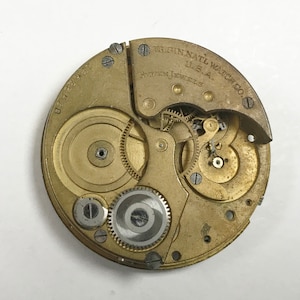 K&ouml;nnte beinhalten: Nahaufnahme eines goldfarbenen Taschenuhrwerks mit der Aufschrift "ELGIN NATL WATCH CO. U.S.A. SEVENTEEN JEWELS" und der Nummer "8388391".