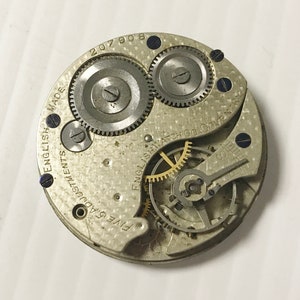 Puede incluir: Primer plano de un movimiento de reloj de bolsillo plateado con el texto "English Watch Co. Coventry" y "Five Adjustments English Made 207908".