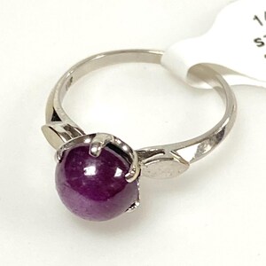 May include: A silver ring featuring a large, oval, deep purple gemstone. The ring's band has a simple design with leaf-like accents on either side of the gemstone. The gemstone is securely held in place by prongs.