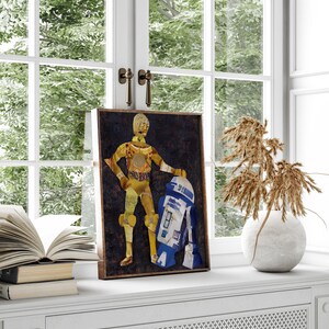 May include: A framed collage art print featuring a gold robot character from Star Wars, C-3PO, standing next to a blue and white robot, R2-D2. The background is a dark brown color.