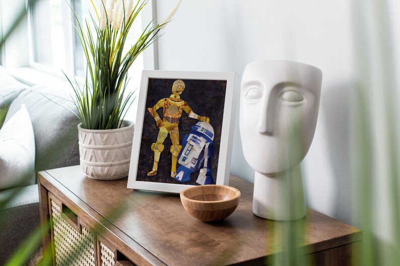 May include: A framed collage of Star Wars characters C-3PO and R2-D2 made from recycled materials, displayed on a wooden table with a white ceramic sculpture and a potted plant.